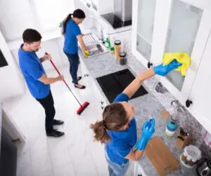 Professional cleaners completing a move-out cleaning in a kitchen, wiping cabinets and cleaning floors before final inspection